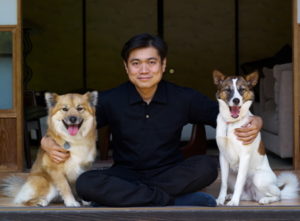 Joi Ito sitting with his arms around two dogs.