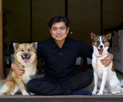 Joi Ito sitting with his arms around two dogs.
