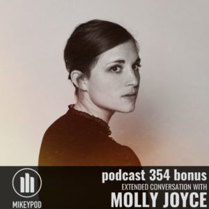 Black and white portrait of Molly Joyce. She has long dark hair which is pulled back. She is gazing toward the right of the camera over her right shoulder toward the camera. There is a black bar at the bottom of the image containing the text "Podcast 354 Bonus; extended conversation with; Molly Joyce"