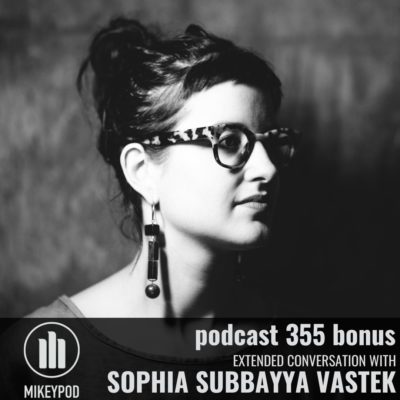 Black and white portrait of Sophia Subbayya Vastek looking to the right of the frame. She is wearing funky-chic leopard glasses, dangling earrings, and her hair is up in a messy bun.